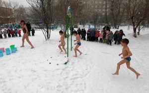 Three children run in snow wearing bathing suits